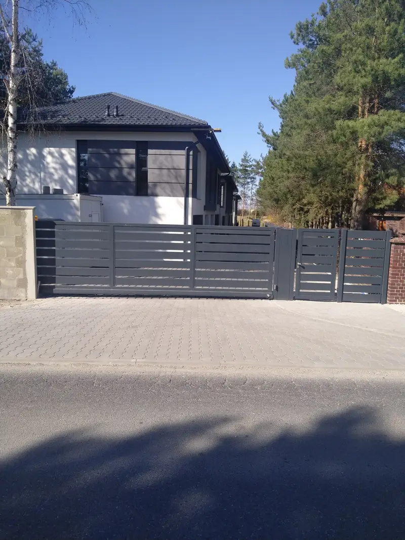 Grafitowa brama i furtka z poziomych profili przed domem wśród sosen