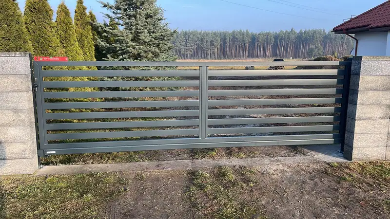 Przęsło z szerokich poziomych profili na bloczkach, w tle las